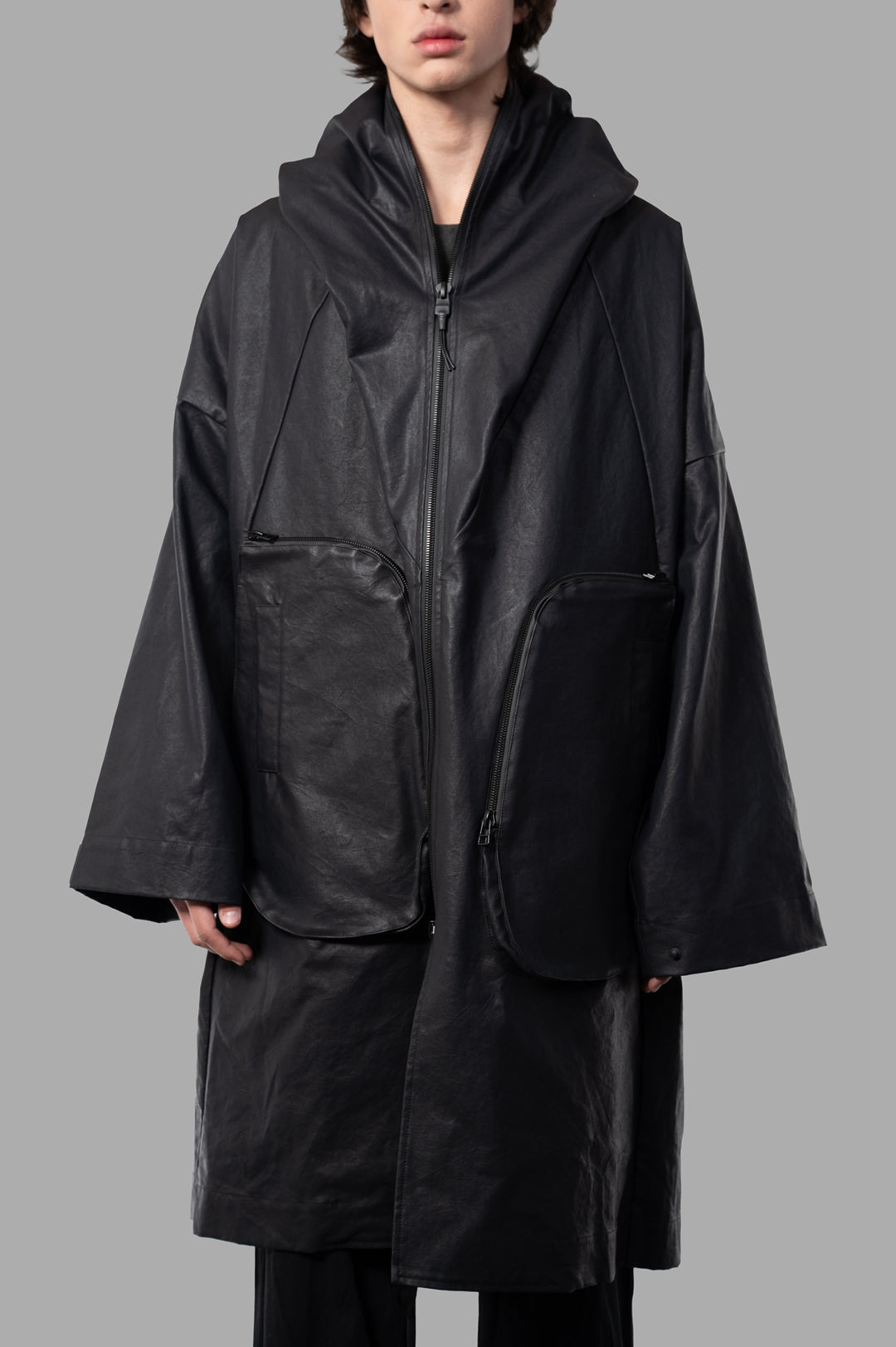 Justin Gall Coated Bodybag Parka, knee-length with large shawl collar and 3D zip pockets, styled in black on model.