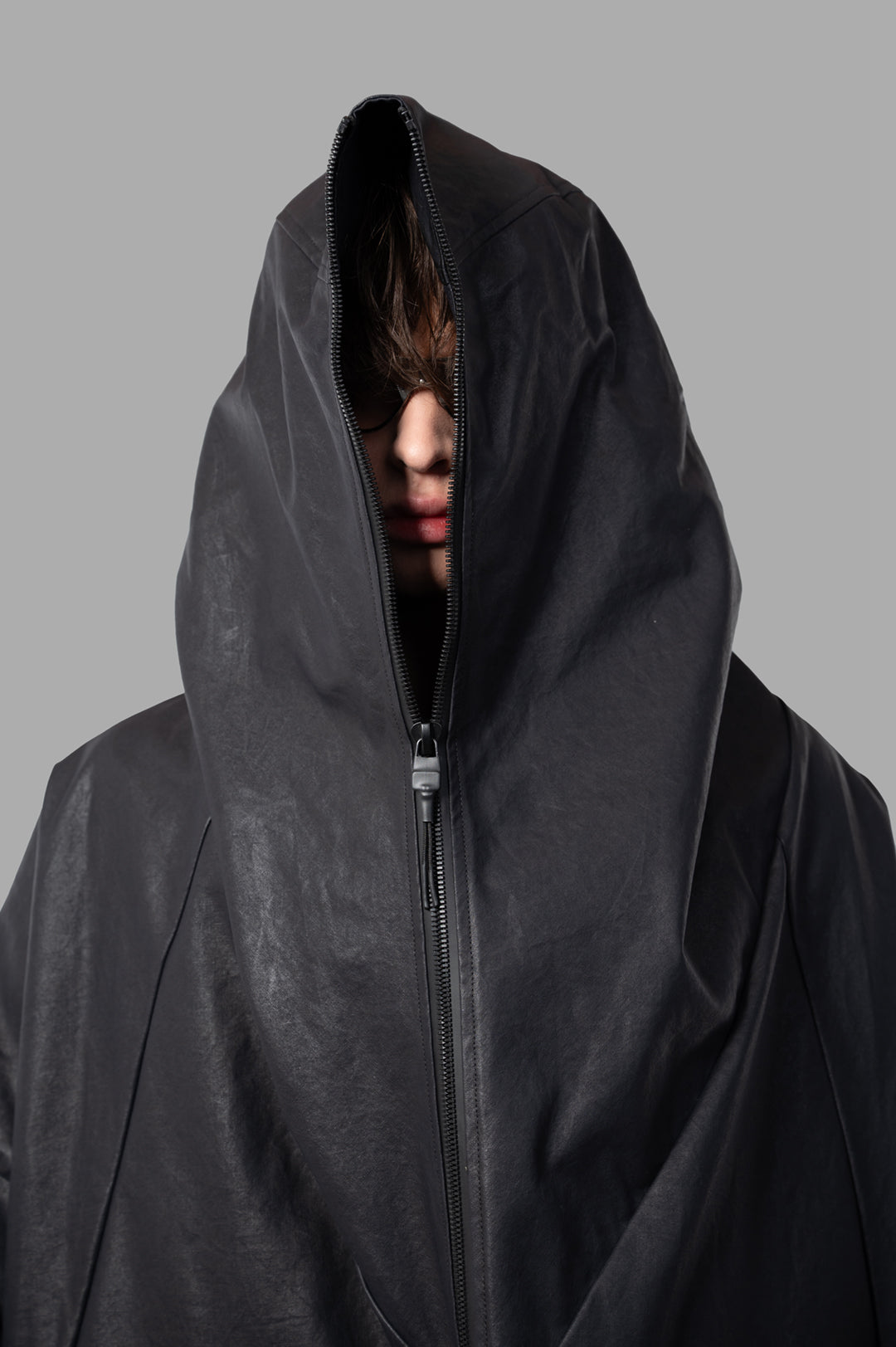Justin Gall Coated Bodybag Parka featuring a dramatic hood and sleek design, showcasing textured fabric and unique zip details.