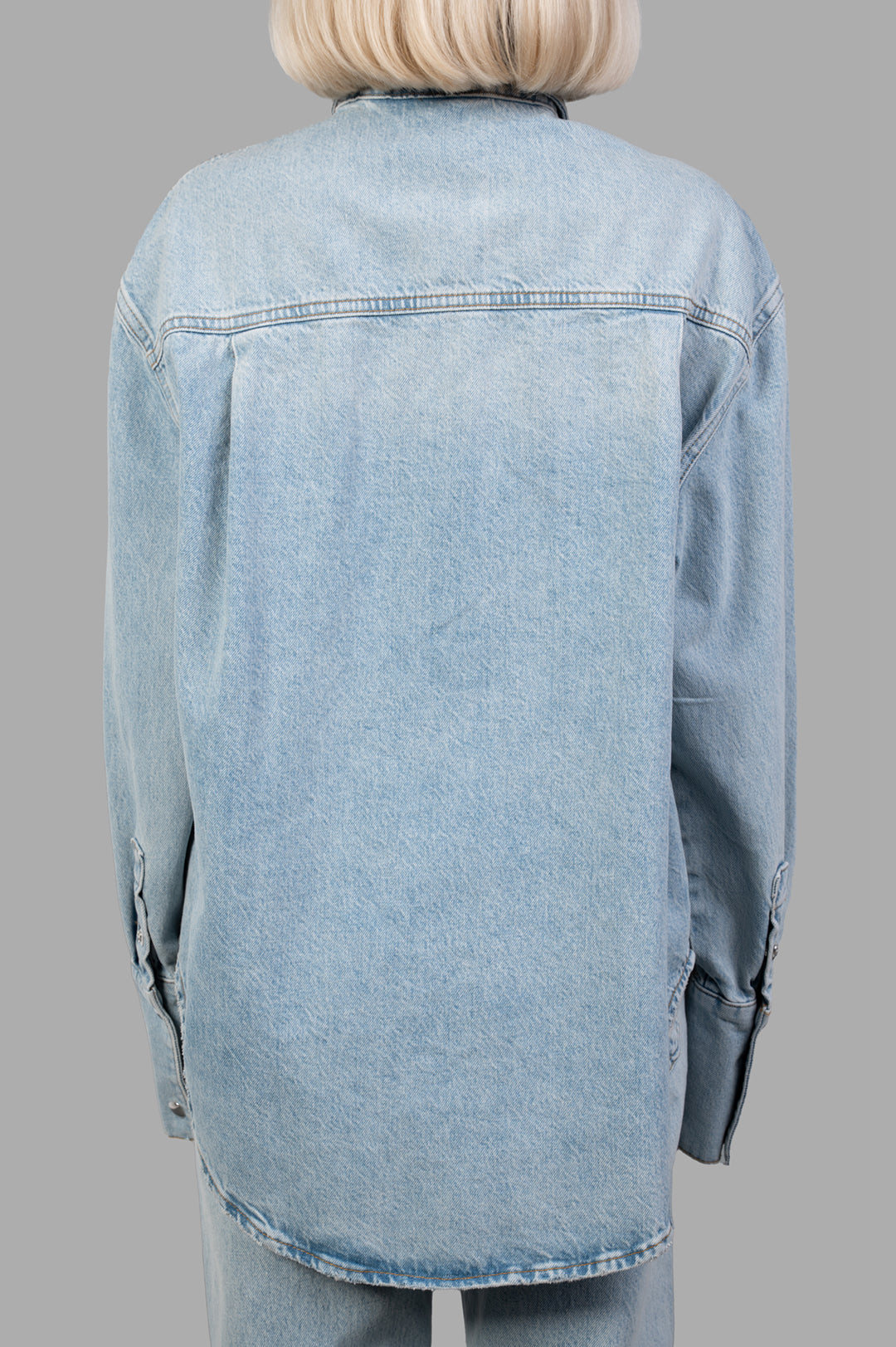 Anine Bing Dante Denim Shirt features a distressed, light blue back view showcasing wide cuffs and signature snap buttons.