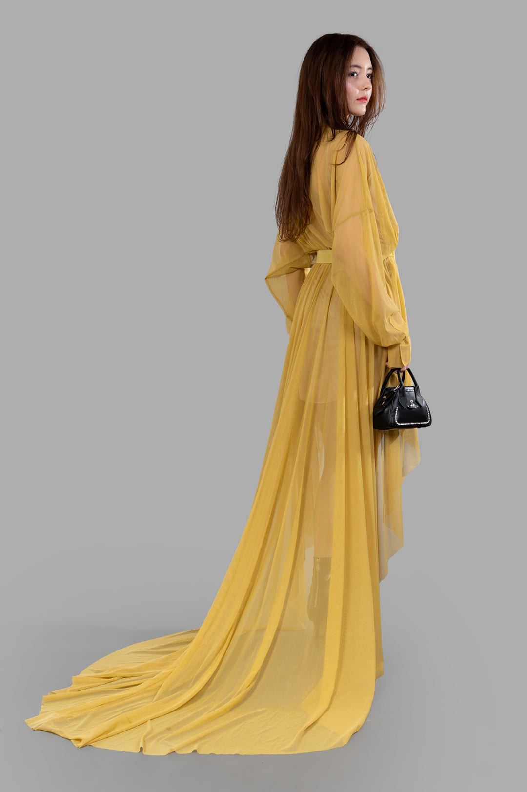 Norma Kamali Belted Shirt Gown, side view, model facing left, long yellow sheer fabric flowing on the floor.