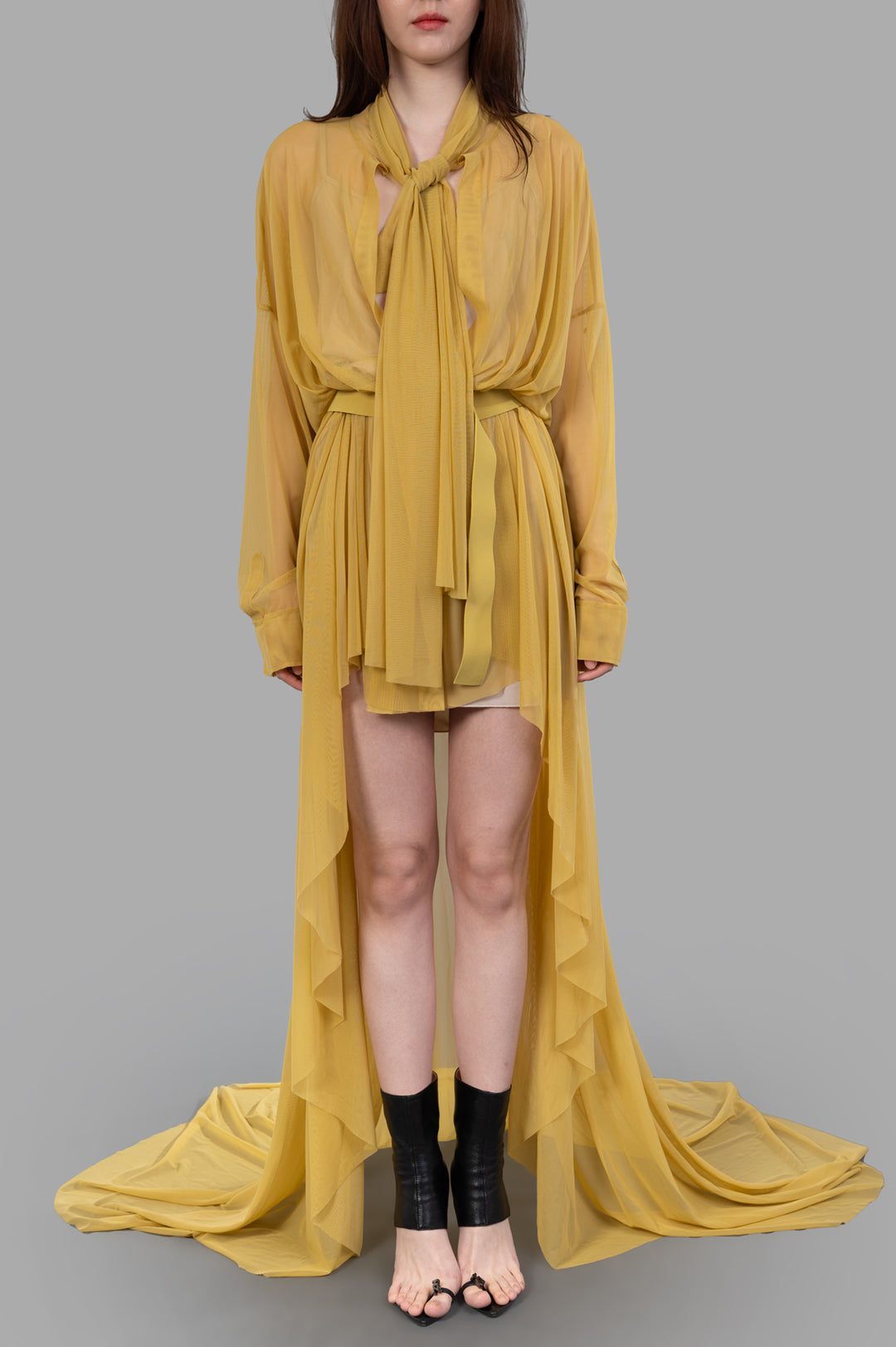 Norma Kamali Belted Shirt Gown displayed on a model, featuring a flowing yellow design with a tied neckline and side ruffles.