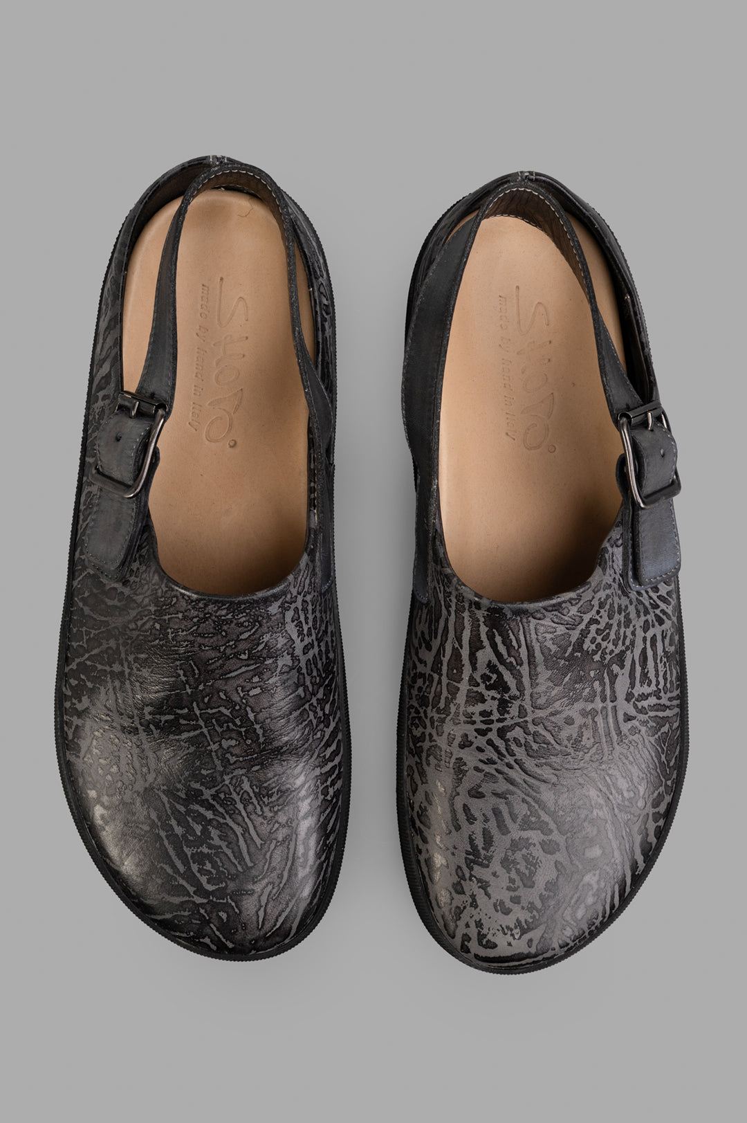 Shoto. Black slip-on mules featuring unique embossed leather texture and adjustable strap, showcasing artisan design and.