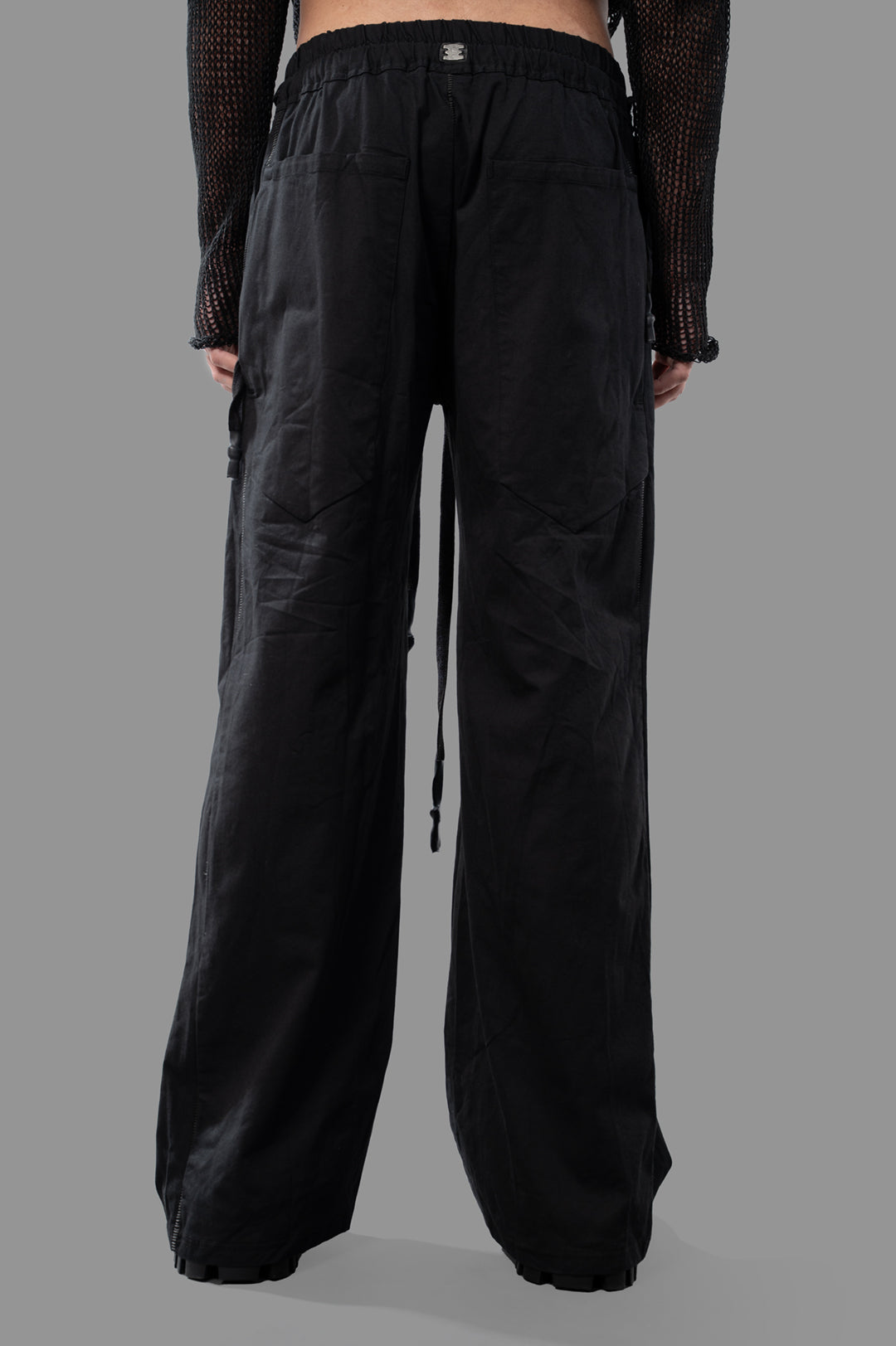 Isaac Sellam Wide-leg Trousers showcase a black design with a relaxed fit, elastic waistband, and detailed back pockets.