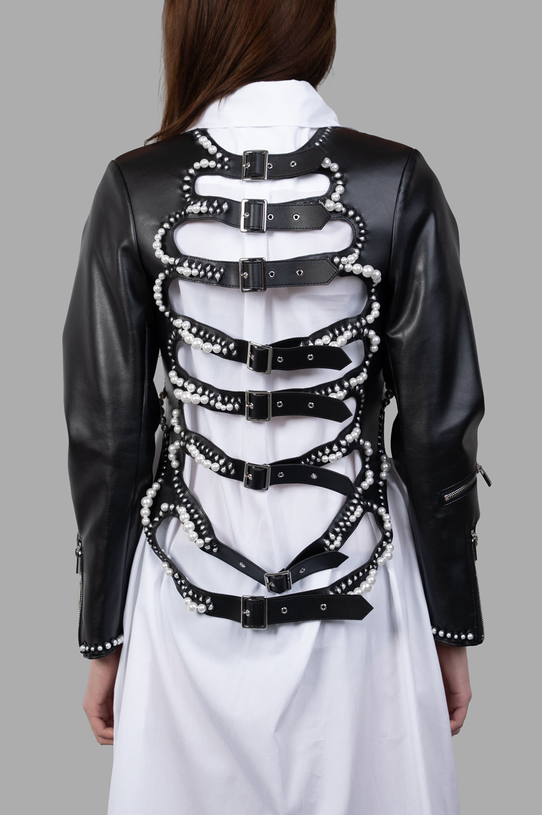 Noir Kei Ninomiya Pearl-Detailed Jacket showcasing back view with adjustable straps and pearl accents on sleek faux leather.