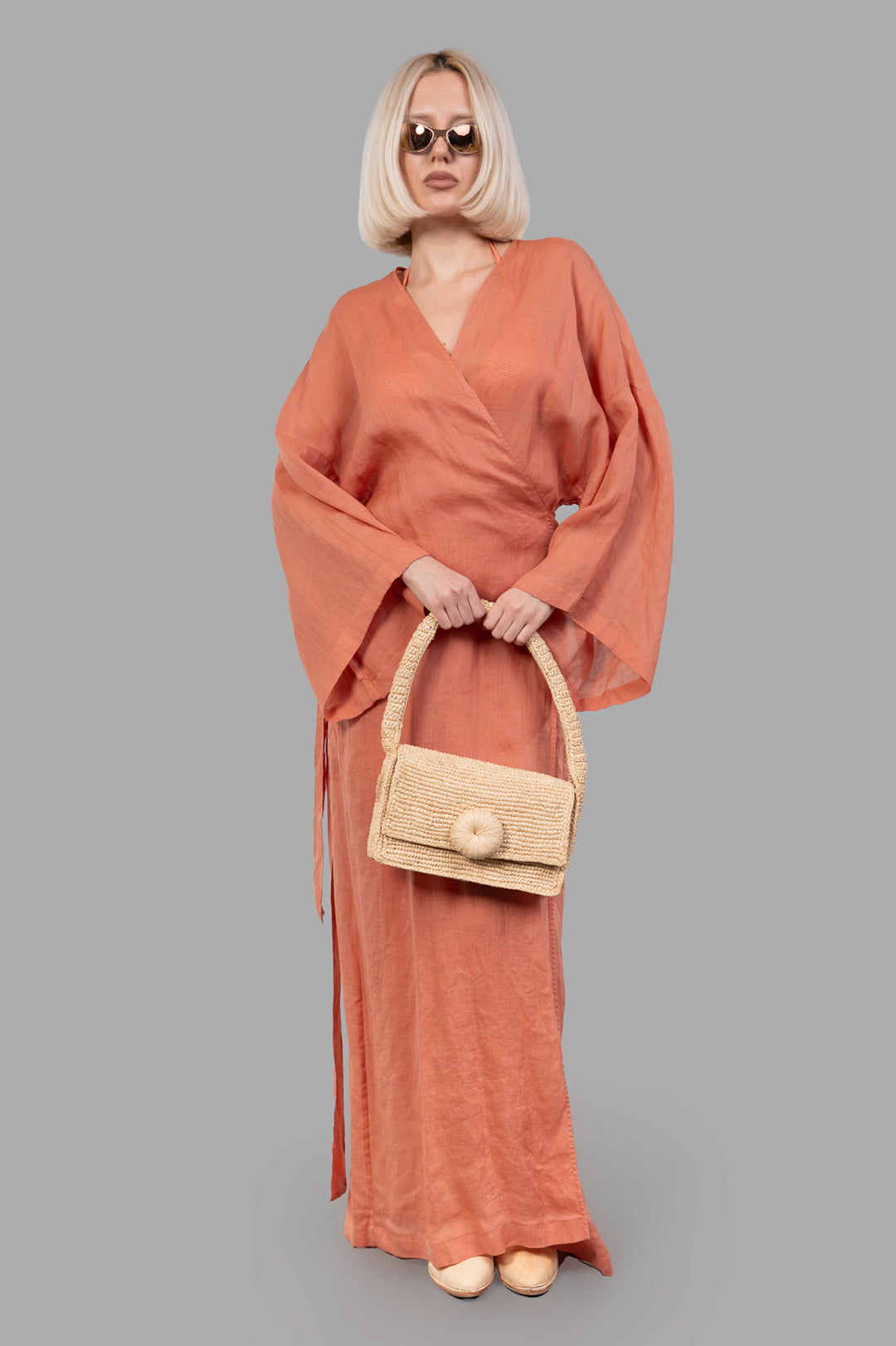 Fisico Pink Kimono with a Frame shown on model, front view. Coral color, maxi-length, sewn-in belt, paired with woven bag.