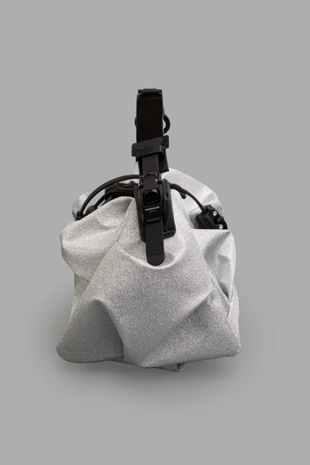 Innerraum Silver Bag I96 features a textured, metallic surface with bold folds and an adjustable black strap.
