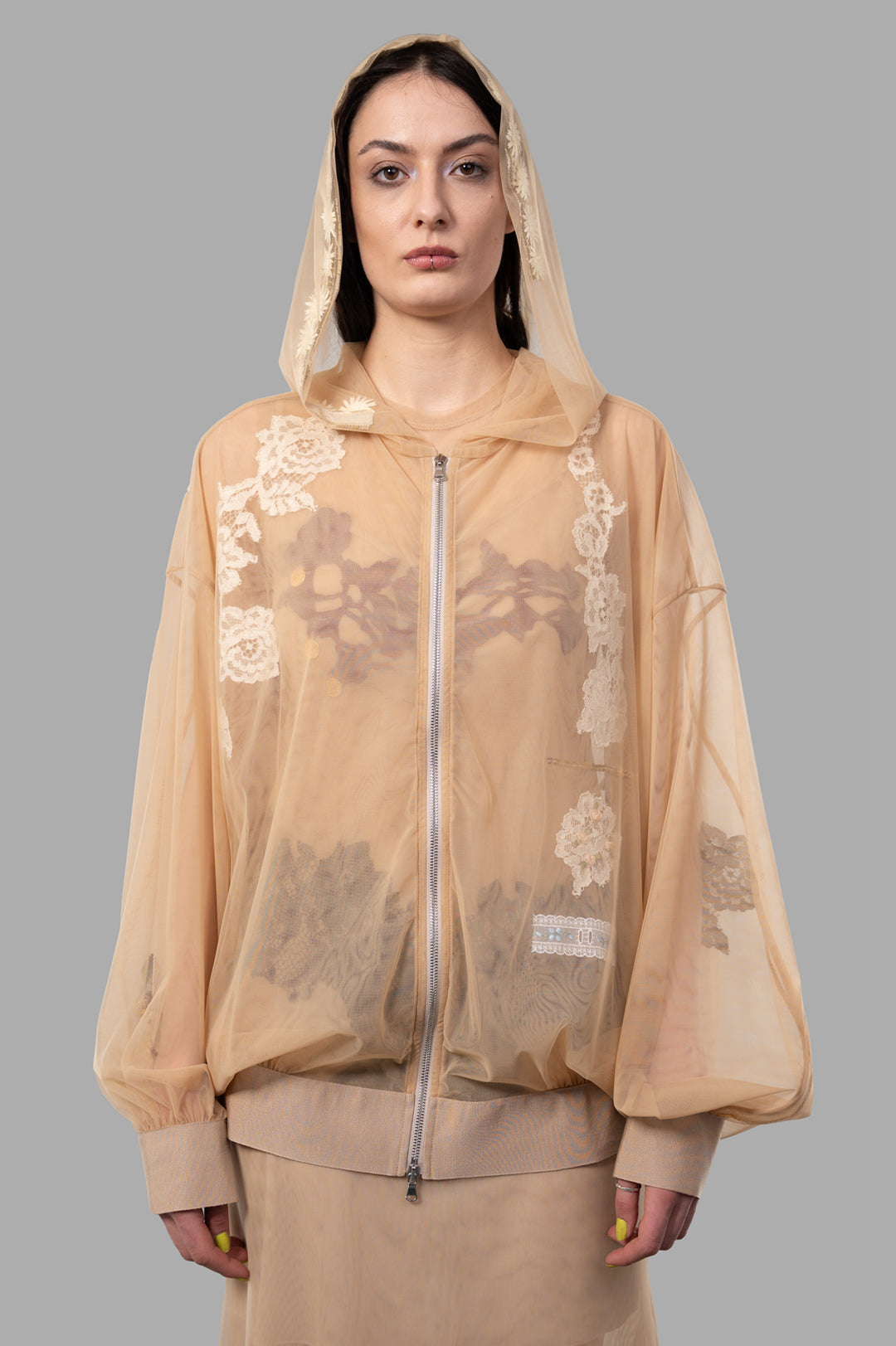 Sehnsucht Atelier. See-through Hoodie in Beige, oversized lace design with hood, showcasing floral embroidery on model.
