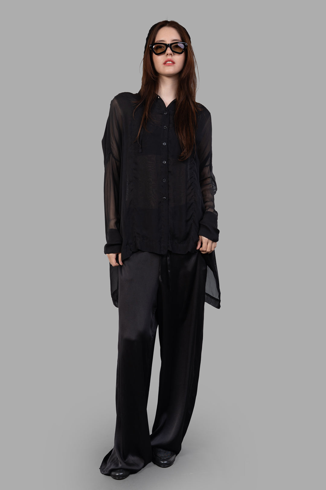 Masnada black silk hooded shirt on-model view, featuring translucent fabric, button closure, and asymmetrical hem.