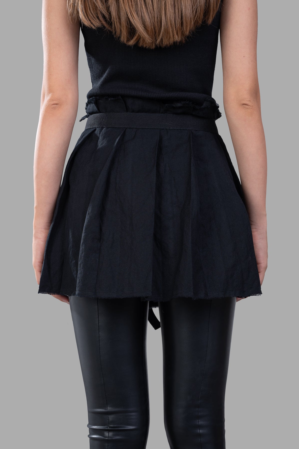 Masnada Self-tie Skirt showcased from the back, featuring pleats in a bold black fabric over sleek black leggings.