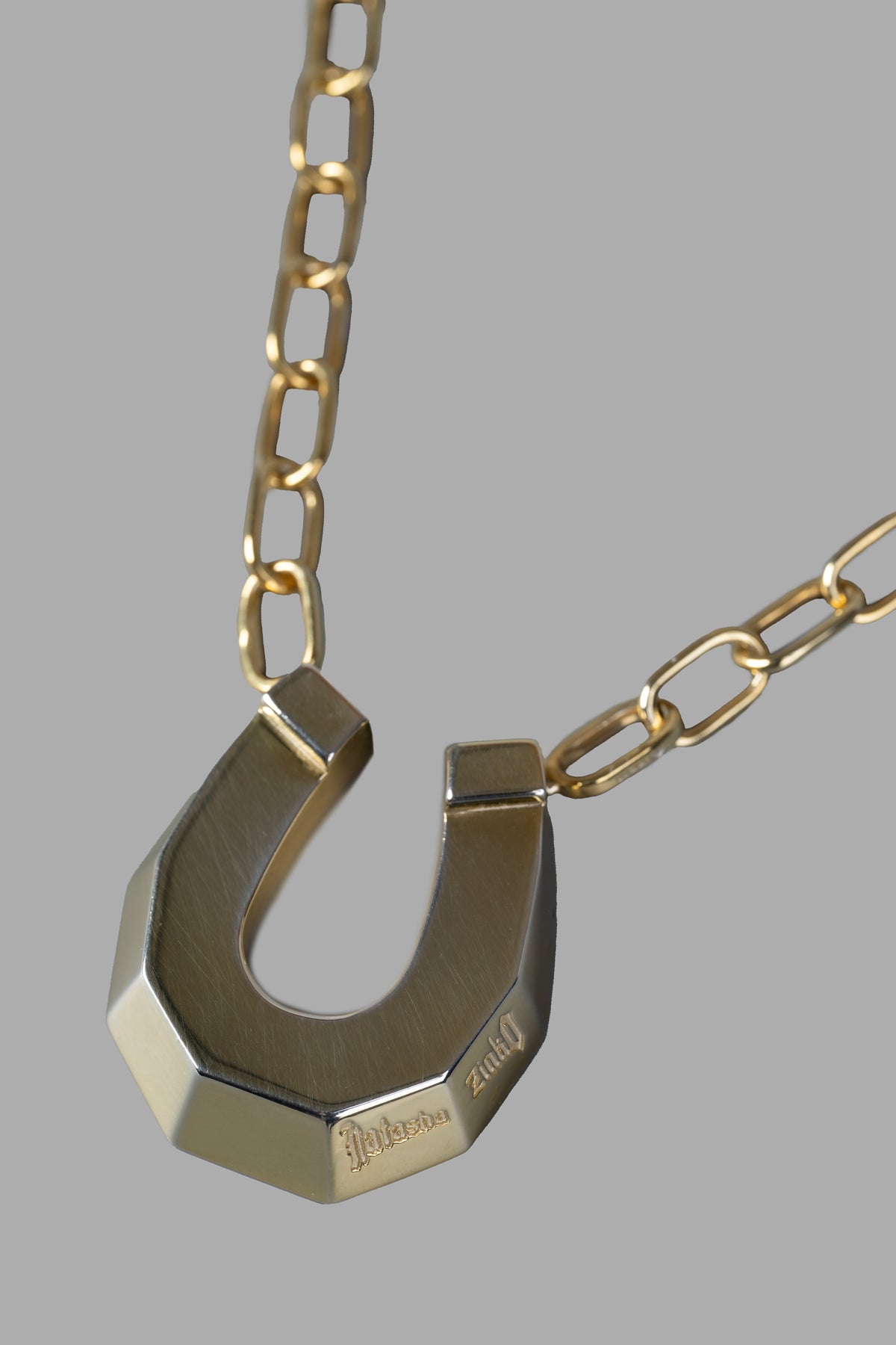 Natasha Zinko Horseshoe Necklace featuring a chunky gold pendant on a chain, showcasing intricate logo engraving.