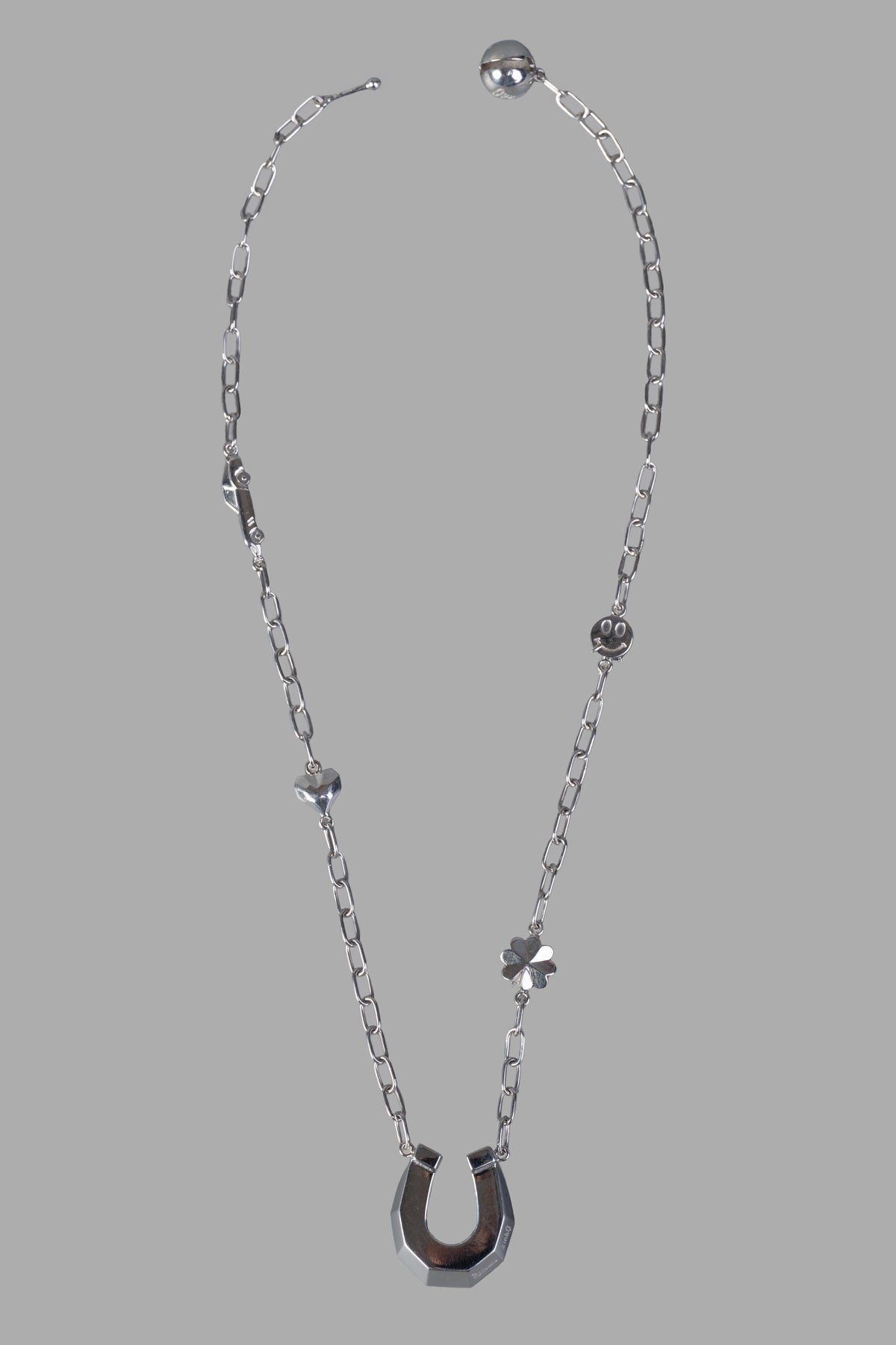 Natasha Zinko silver horseshoe necklace with playful pendants, featuring a logo-engraved horseshoe on a detailed chain.