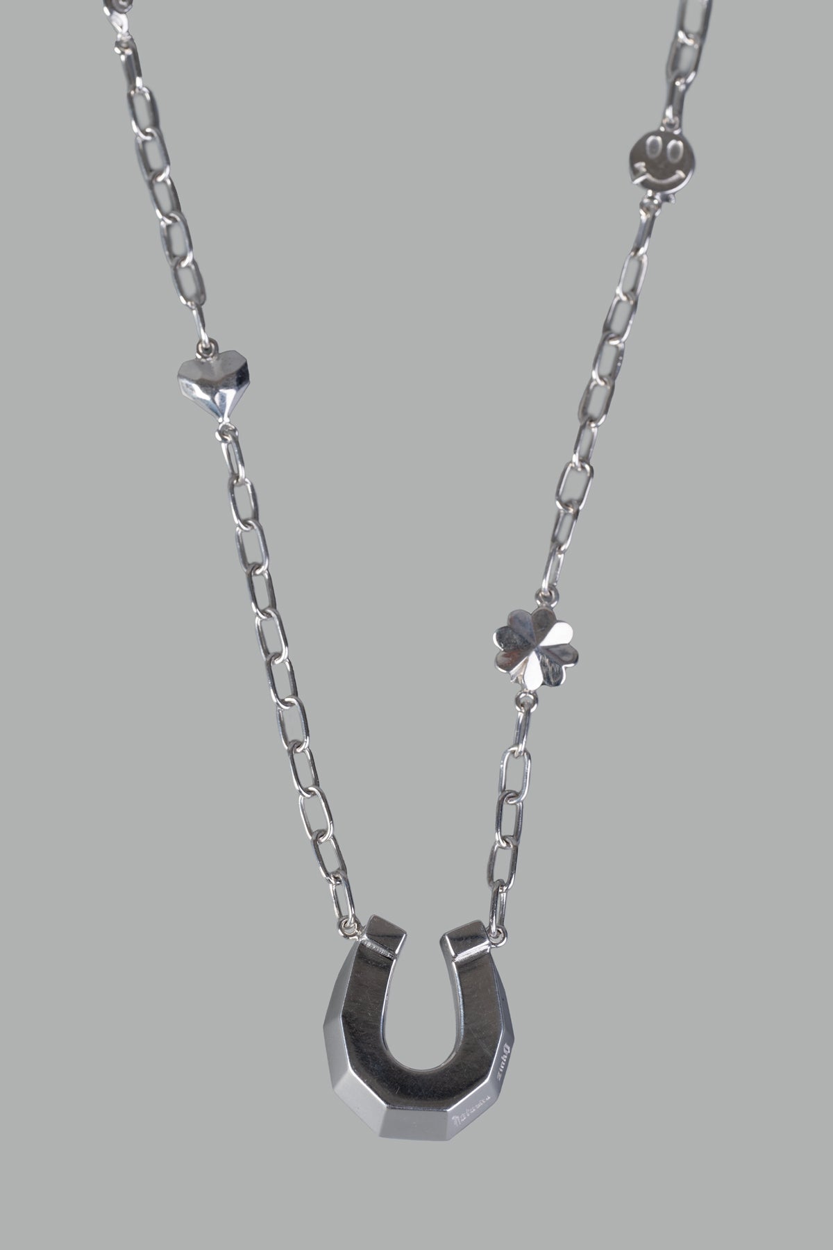 Natasha Zinko Horseshoe Necklace with Pendants showcases a shiny silver horseshoe, heart, and flower details on a chain.