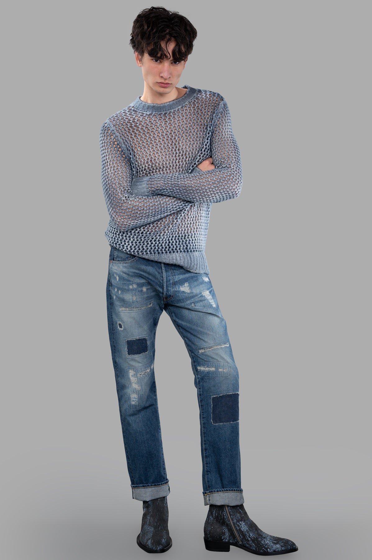 Avant Toi Blue Open-knit Sweater, front view on-model with folded arms, paired with distressed jeans and boots.