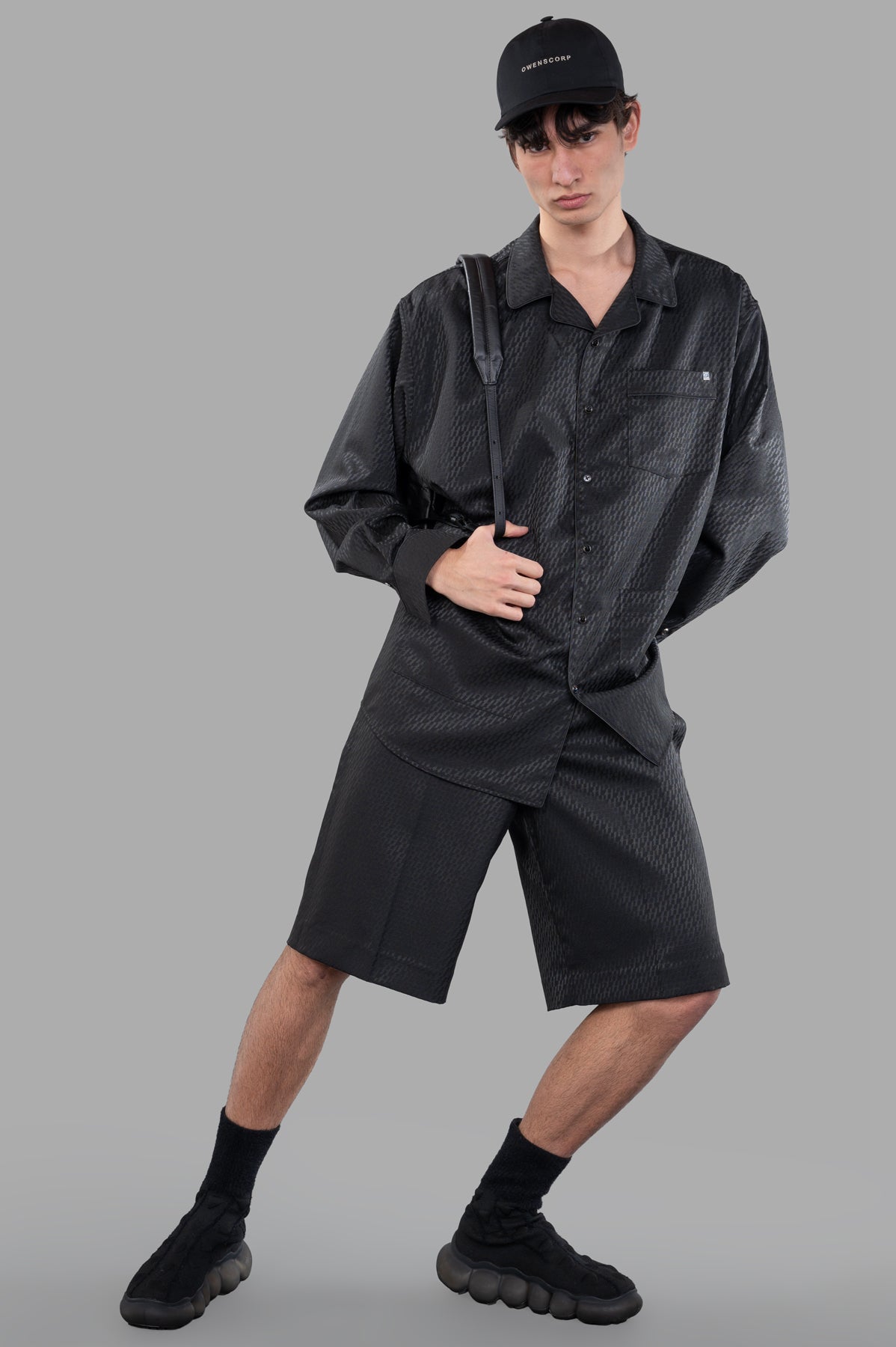 Helmut Lang Oversized PJ Shirt in black satin shown on model, featuring button-front, convertible collar, and piped accents.