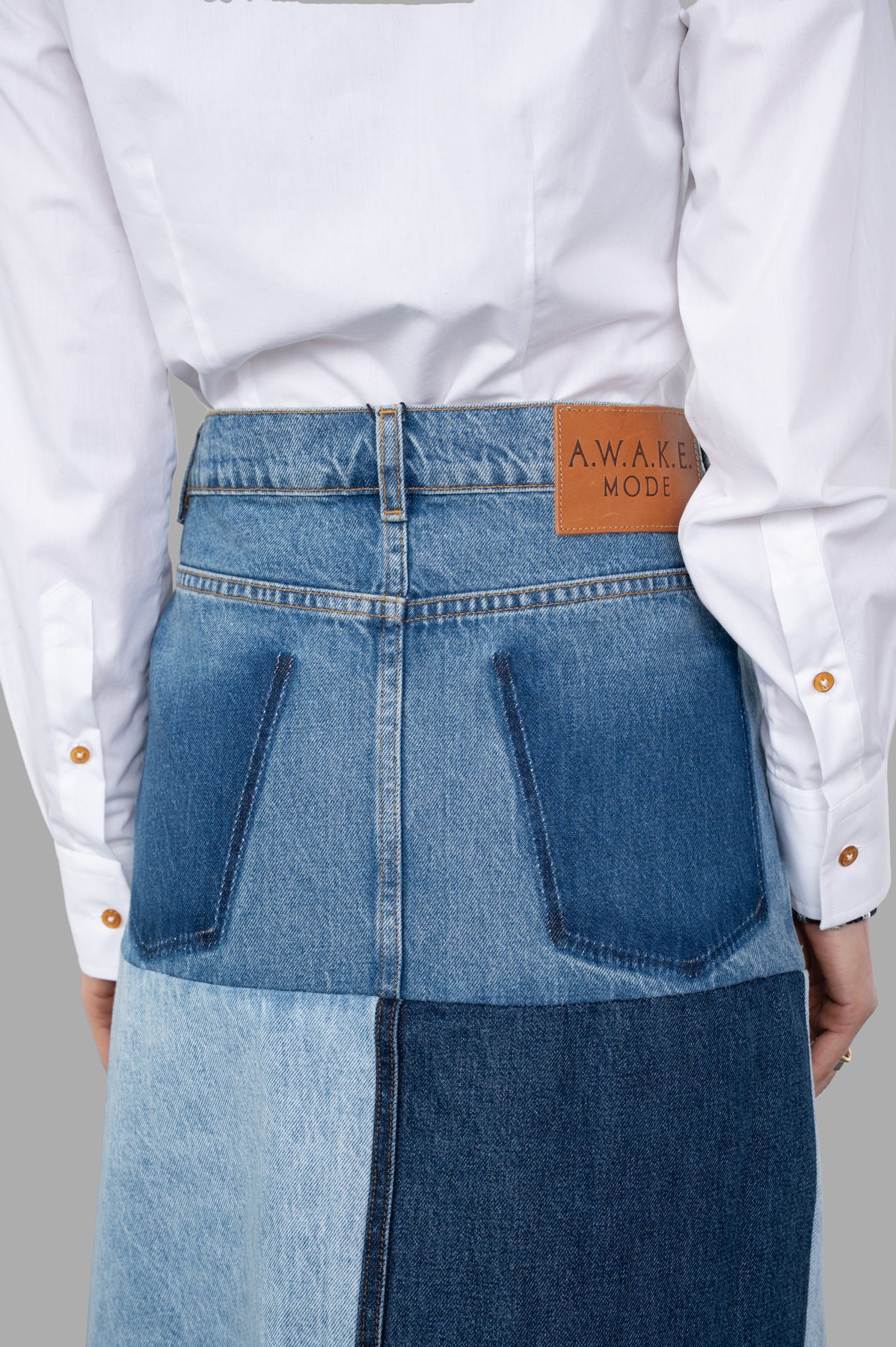 A.W.A.K.E. MODE Mirror-effect Skirt shows back details, featuring a color-block design and signature logo at the waist.