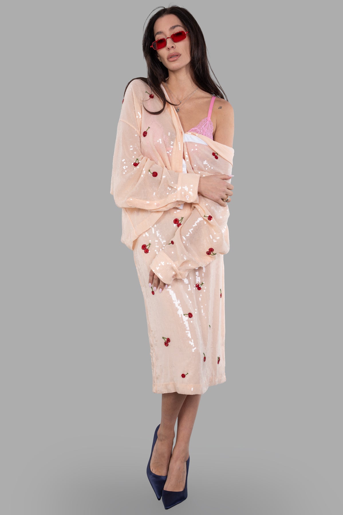 DES PHEMMES pink lace bra peeking under sheer cherry-patterned outfit, front view on-model with red sunglasses.