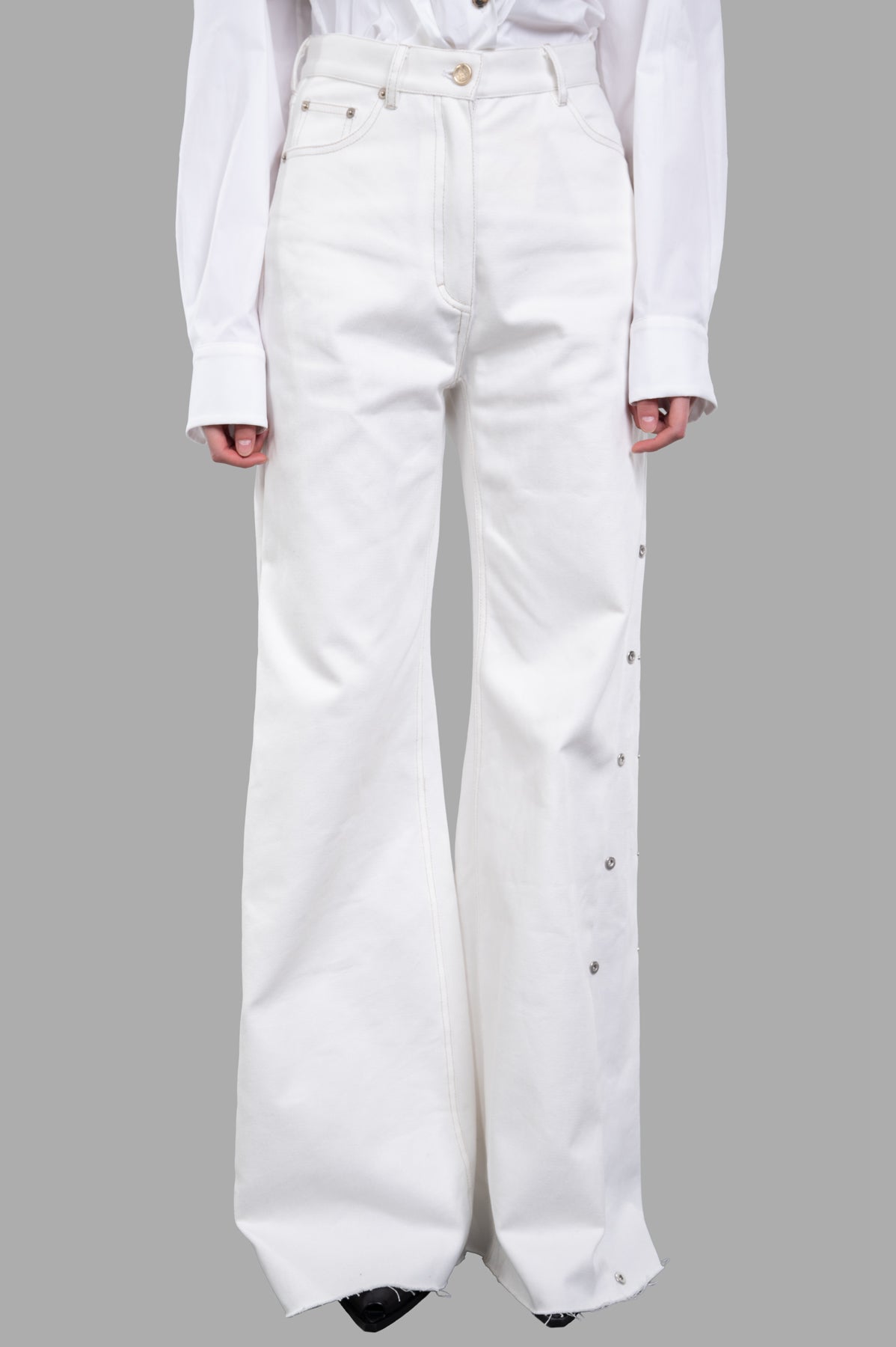 Sehnsucht Atelier Wide-leg Jeans showcase a high-waisted fit with metal-button detailing, styled with a white blouse.