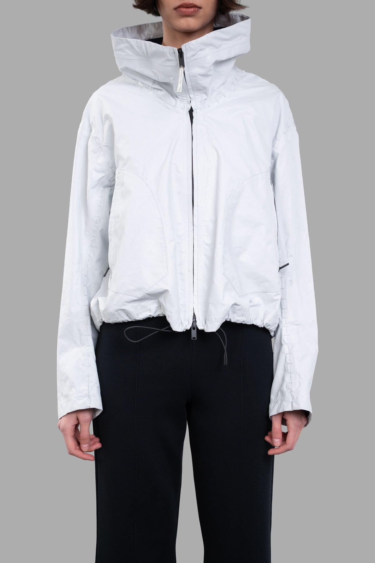 Isaac Sellam Cropped Windbreaker Jacket featuring tube neckline and elastic drawstring, styled in off-white on model.