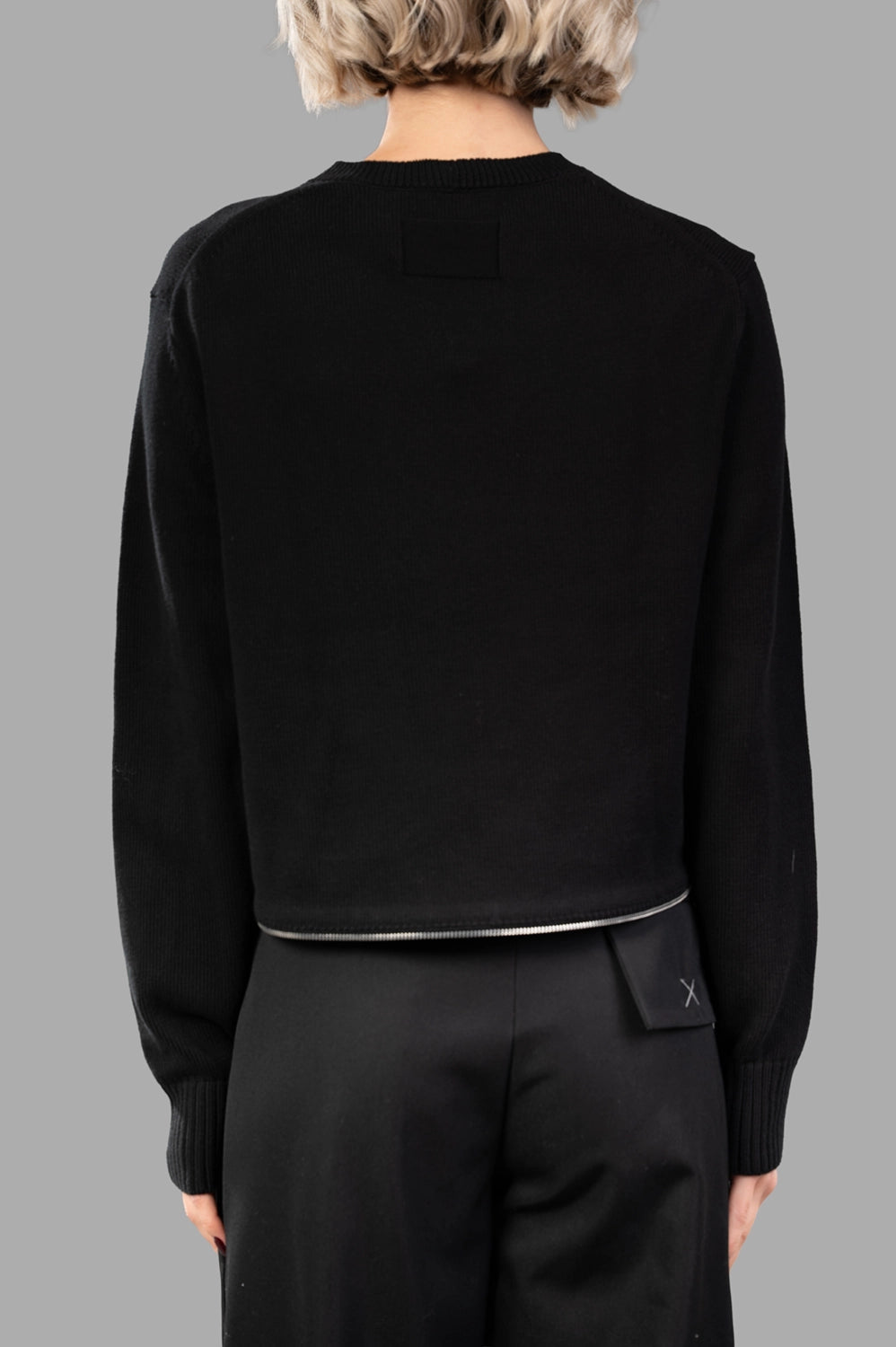 Back close-up of black cropped knit showing zip detail along hem and clean finish