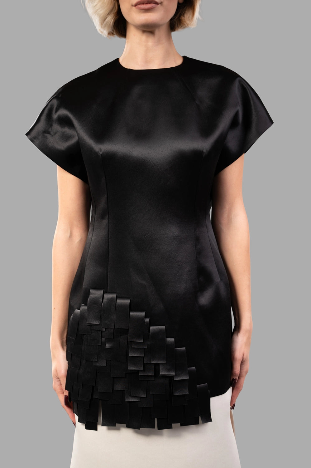 Front close-up of black satin top showing cap sleeves, sculpted seams and layered rectangle appliqués at hem