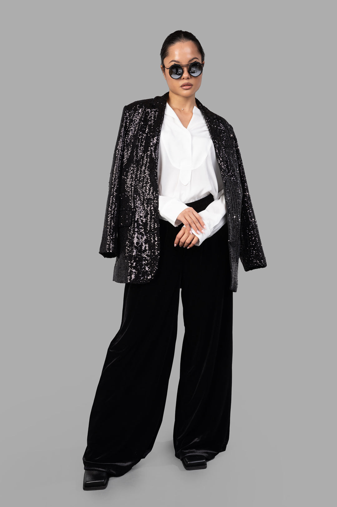 Norma Kamali Wide-leg Velvet Pants in black, on model with white blouse and sequin jacket. Elegant and stylish look.
