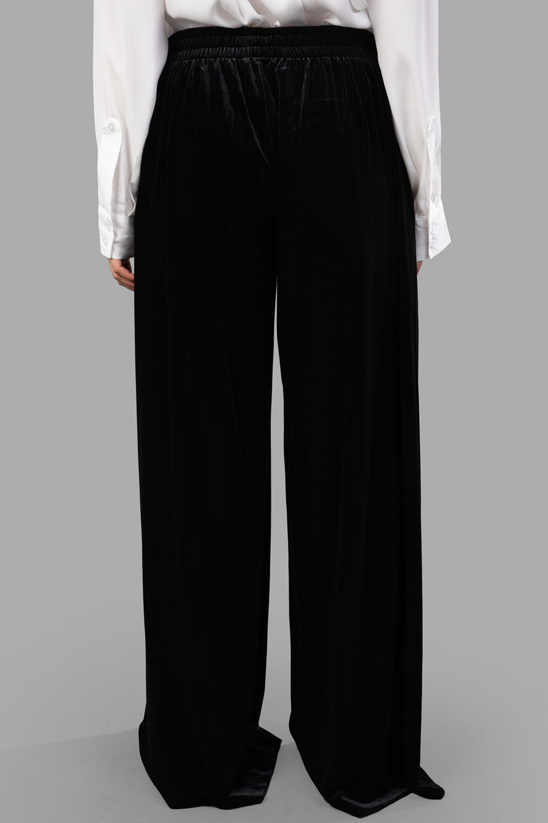 Norma Kamali Wide-leg Velvet Pants shown from the back, featuring an elasticized waist and soft black velvet fabric.