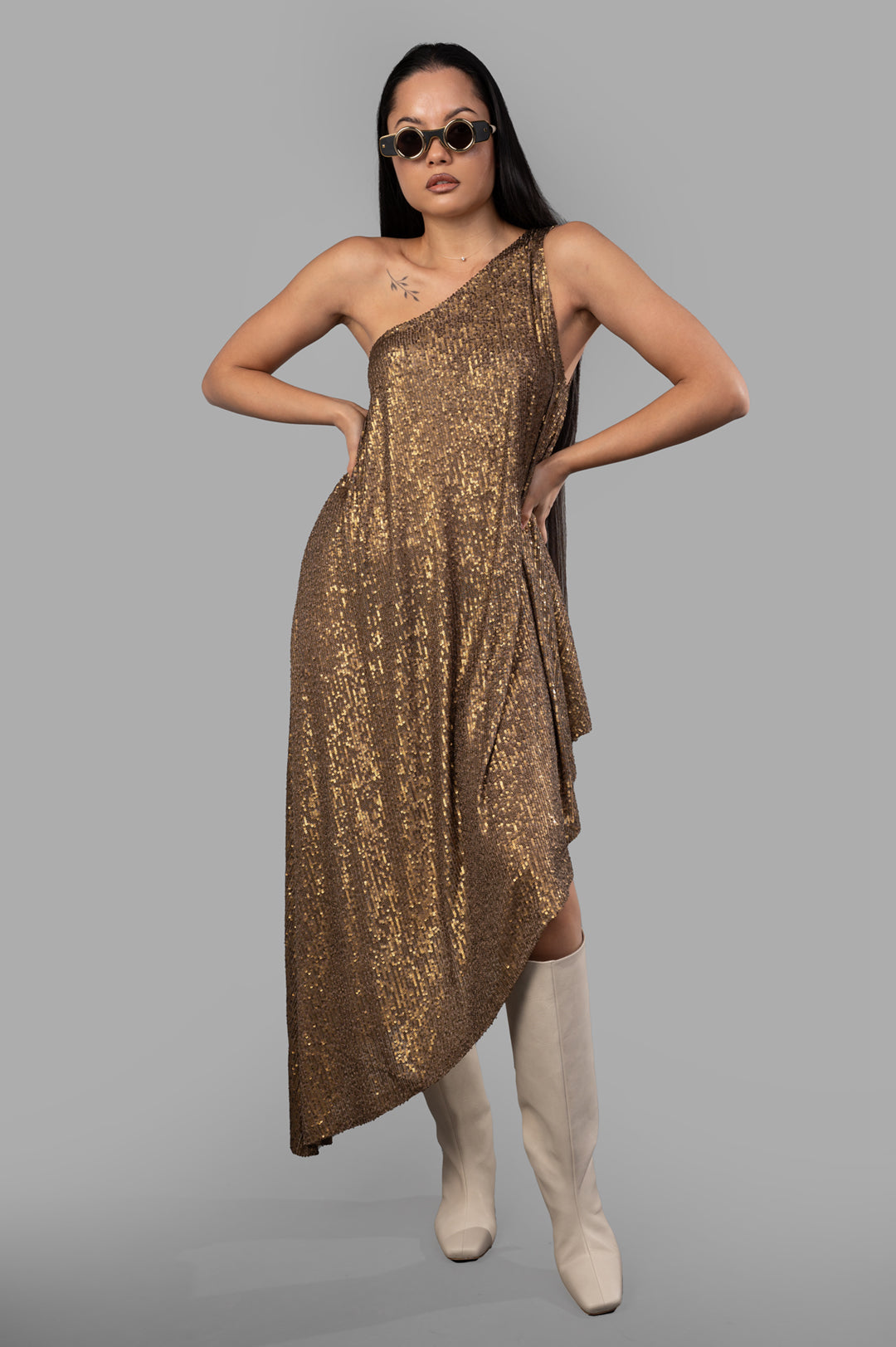 Norma Kamali one-shoulder diagonal tunic, sequin bronze fabric, asymmetrical hem, sleeveless, modeled with boots.
