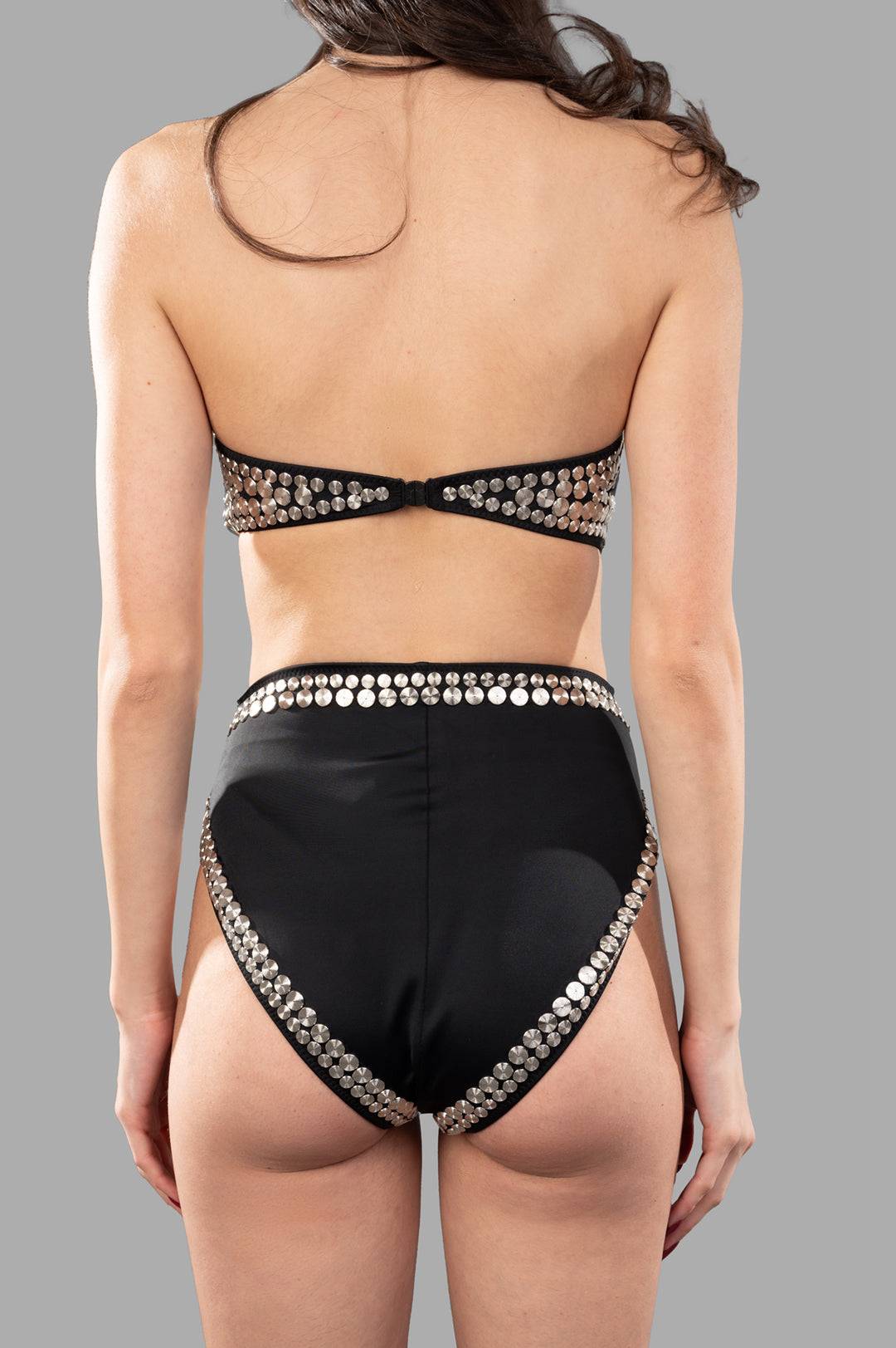 Norma Kamali All-Over Stud Bikinis, showcasing back view with metallic studs, high-waisted design, on model against gray background.