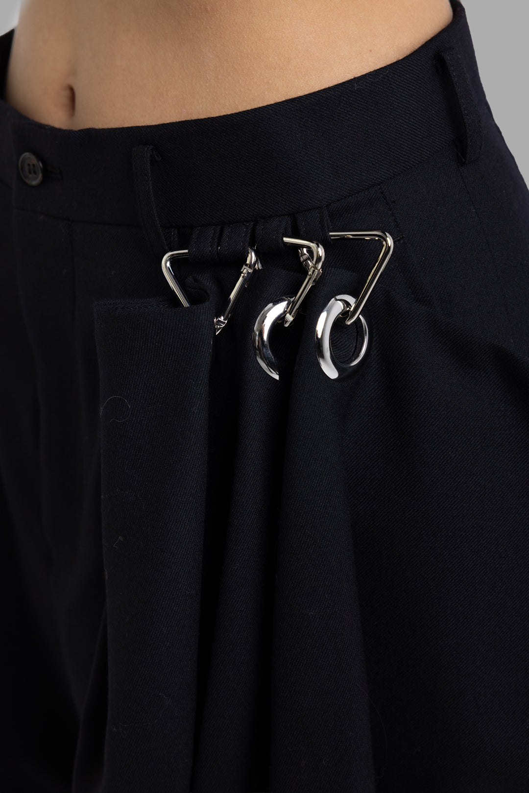 Noir Kei Ninomiya black wool trousers, hardware close-up showing silver carabiners and rings at waistband
